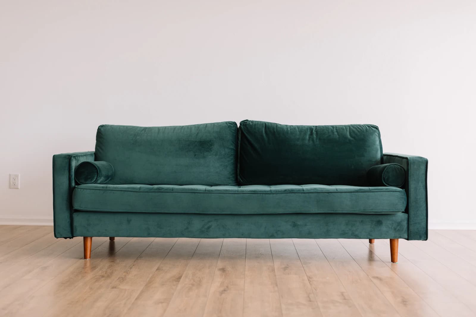 A well-loved green fabric sofa with soft cushions and wooden legs